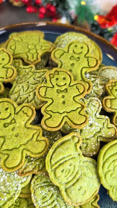 Sablés de Noël au matcha vert jade en forme de bonhommes de pain d'épices et de sapins, empilés sur une assiette