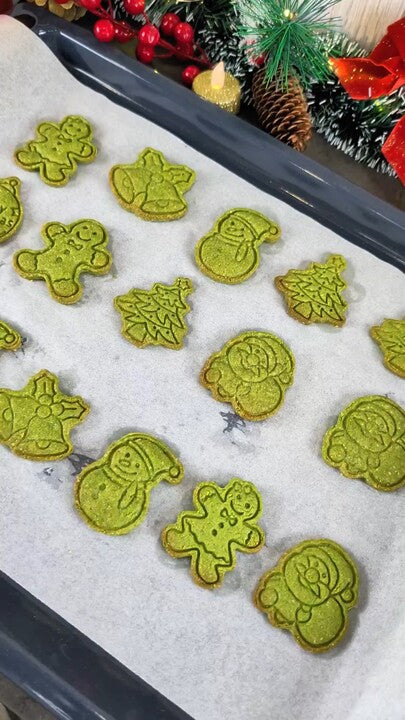 Sablé de Noël au matcha en forme de bonhomme tenu à la main devant une assiette de biscuits verts